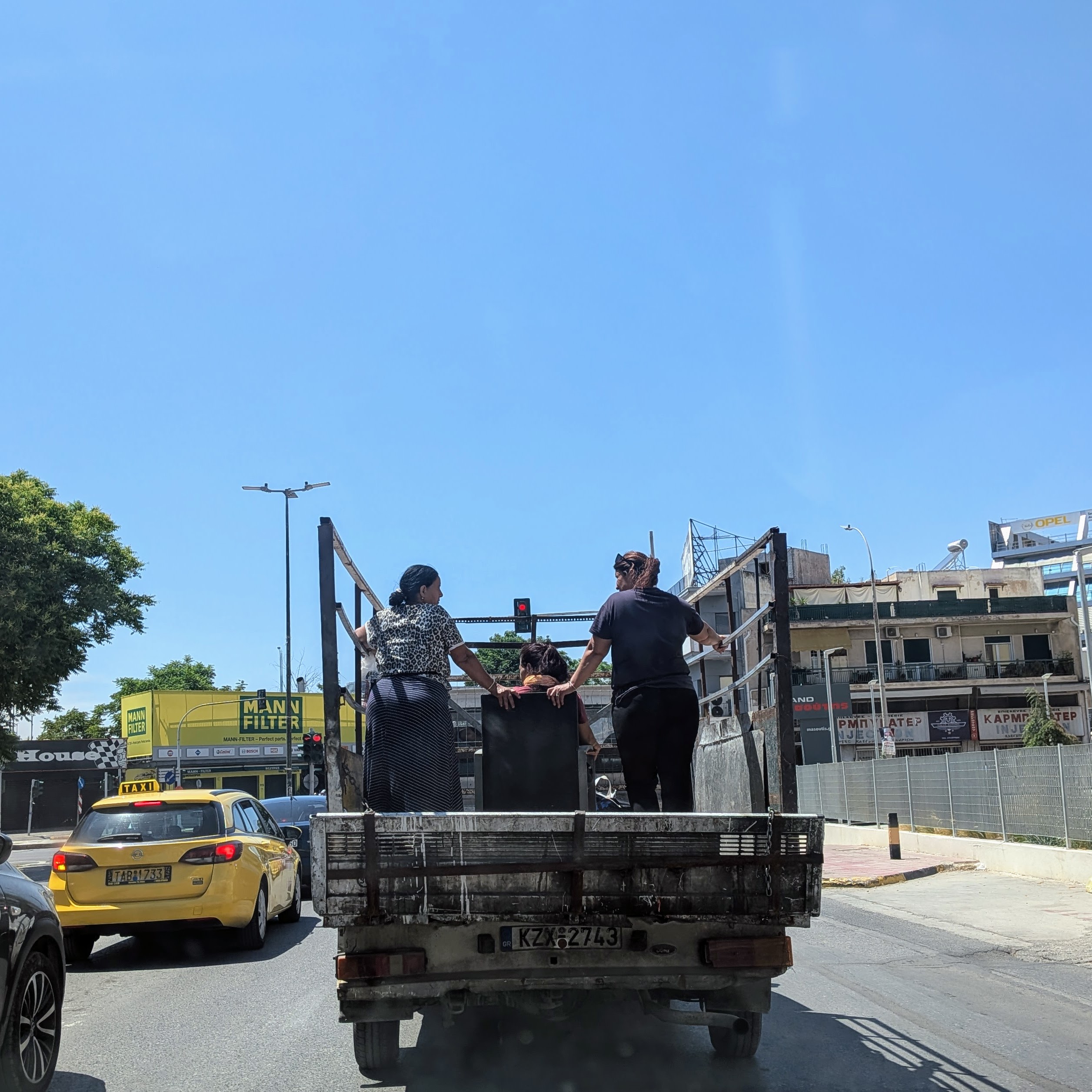 Three women standing on the back of a flatbed truck in Athens traffic